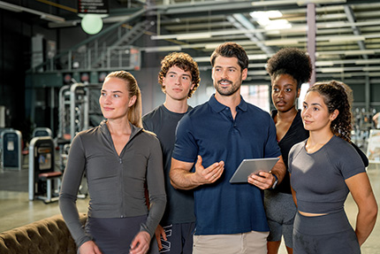 Trainer erklärt einer Gruppe Mitarbeiter:innen, wie es im Fitnessstudio läuft.