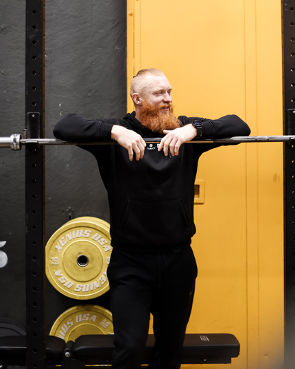 Bärtiger Mann lehnt lässig über einer Gewichthebestange