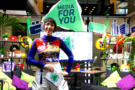 Frau im schrill-bunten T-Shirt vor ihrem Messestand "Media for you"